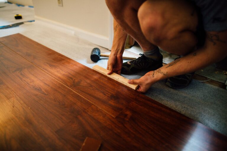 Worker installing laminate wood floor planks with a mallet